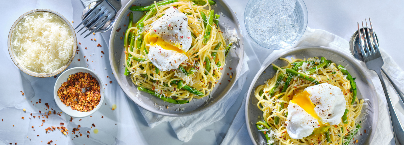 Green bean carbonara in bowl with a bowl of parm cheese and a small bowl of chilli flakes beside it