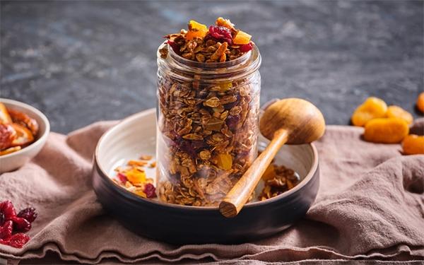 Molasses Cinnamon Granola in a mason jar on top of a bowl with a wooden spoon beside it