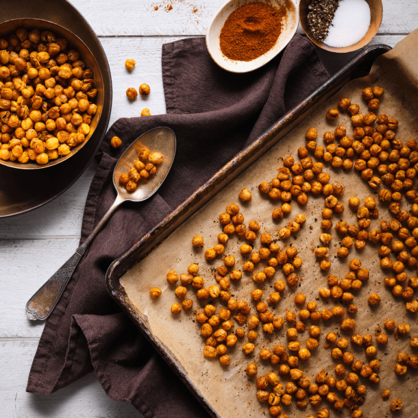 Roasted chickpeas on a baking pan with more chickpeas in a bowl beside it