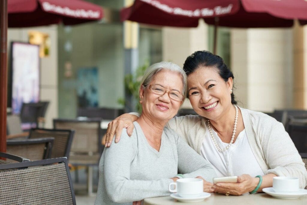 Two women smiling over tea while one has her arm around the other woman