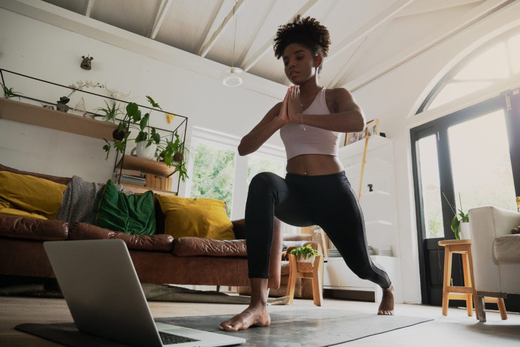 Wide angle shot of young mixed race female doing home workout or yoga from home, following an online workout on computer or online. 