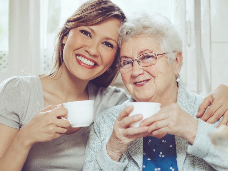 Une femme et une aînée sourient, une tasse de thé à la main.