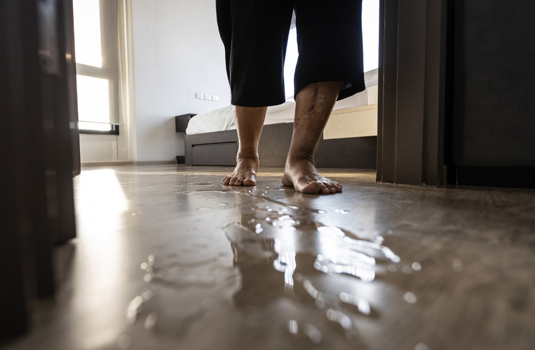 Puddle of water on floor and an older lady walking towards it barefoot
