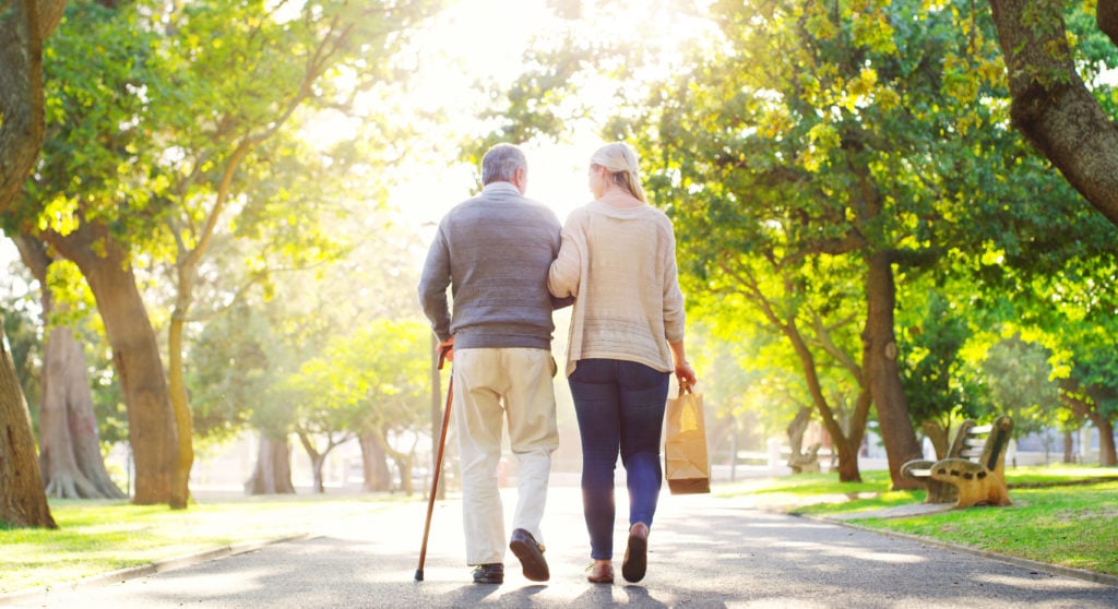 Rearview shot of a young woman assisting her senior father walk at the park