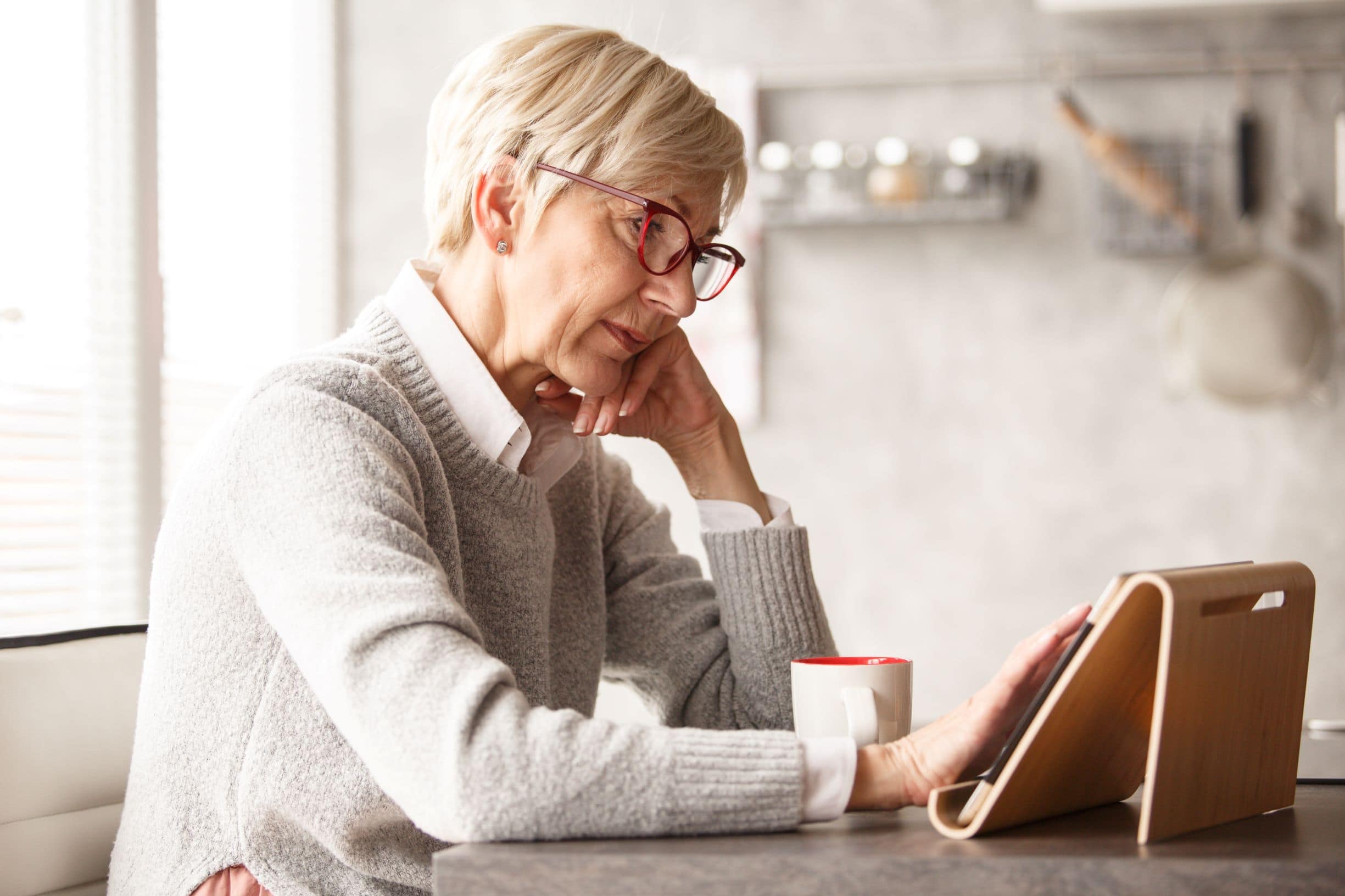 Older woman having a coffee or tea while using her tablet