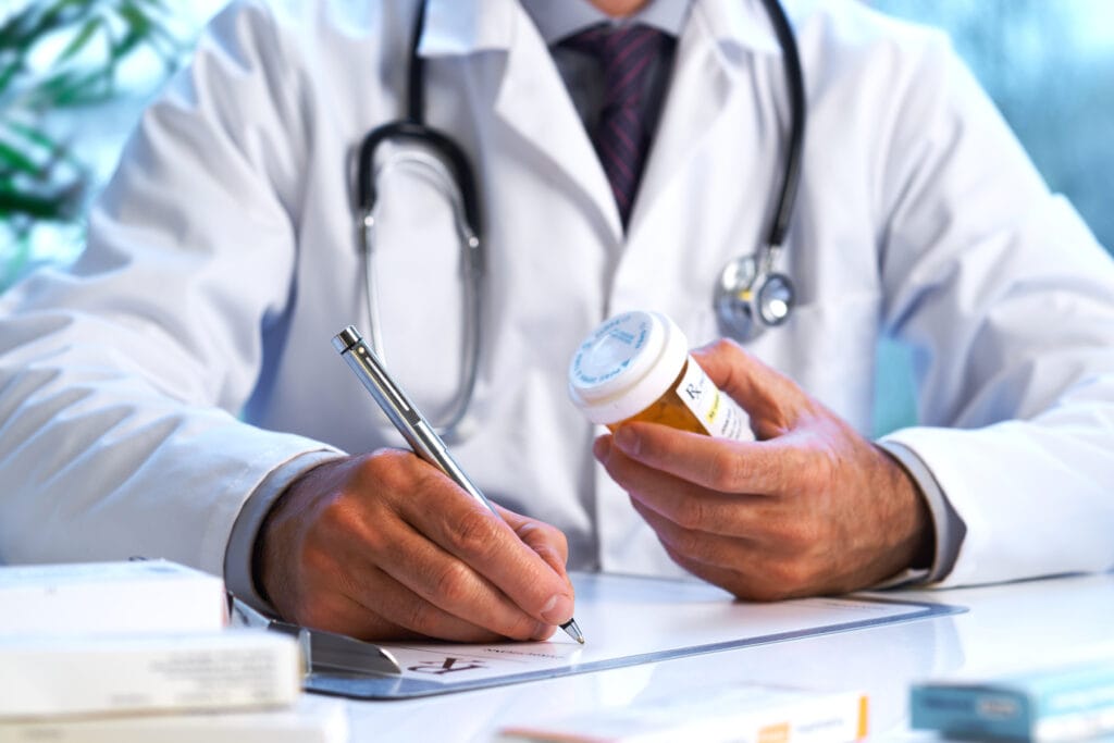 Gros plan d’un médecin rédigeant une ordonnance en tenant une bouteille de pilules à la main.