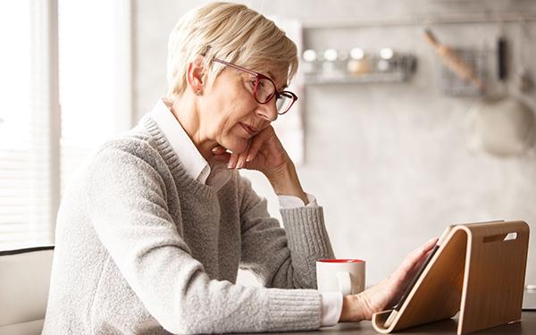 Older woman having a coffee or tea while using her tablet