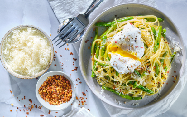 Green bean carbonara in bowl with a bowl of parm cheese and a small bowl of chili flakes beside it